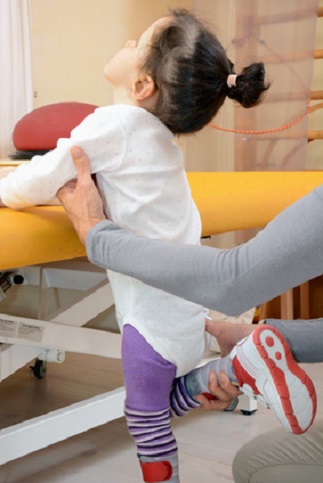 Die Physiotherapeutin hilft einem Kind bei seinen Knieübungen.