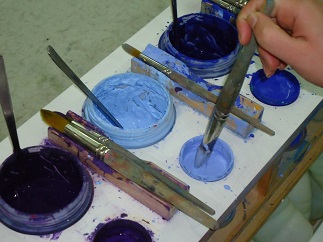 Eine Person taucht den Pinsel in den Farbtopf, um danach zu malen.