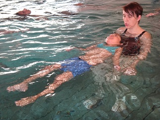 Ein Mitglied liegt mit dem Rücken im Wasser des Hallenbads und wird von der Therapeutin gehalten.