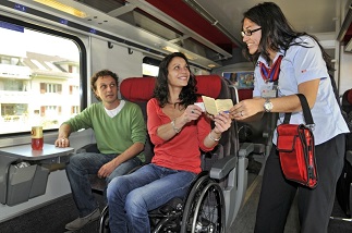 Eine Kondukteurin kontrolliert bei einer Dame im Rollstuhl die Ausweiskarte für Reisende mit einer Behinderung.